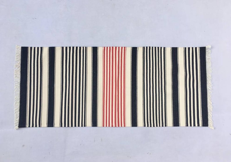 May include: A striped rug with black, white and red stripes. The rug has a fringe on both ends.