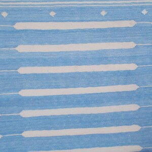 Puede incluir: Una alfombra de rayas azules y blancas con un patr&oacute;n geom&eacute;trico. La alfombra tiene un brillo sutil y una textura suave.
