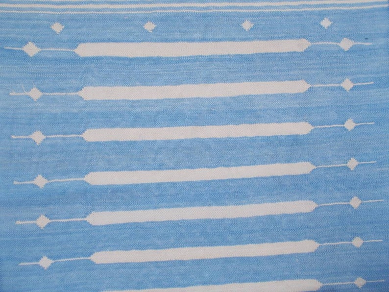 Puede incluir: Una alfombra de rayas azules y blancas con un patr&oacute;n geom&eacute;trico. La alfombra tiene un brillo sutil y una textura suave.