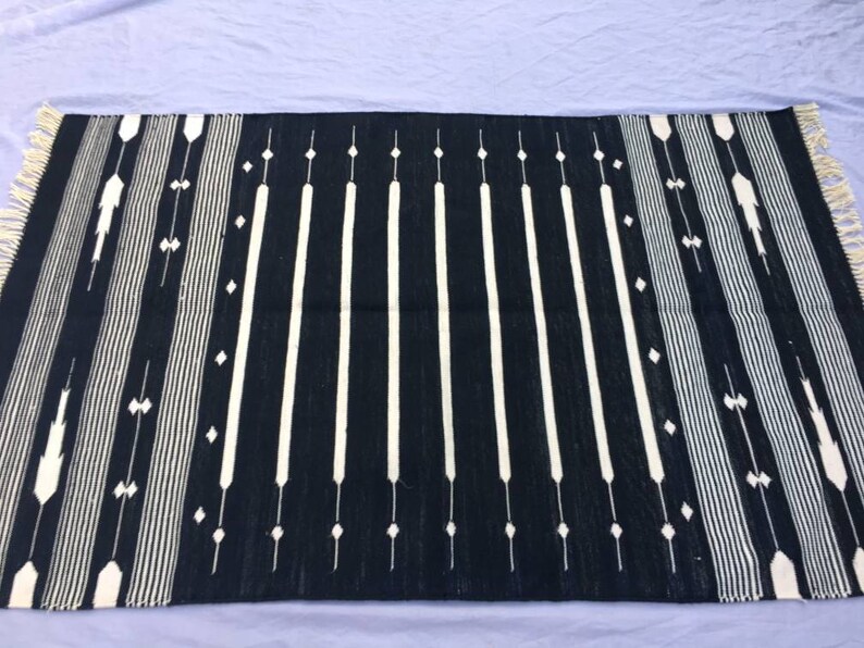 May include: Black and white striped rug with a geometric pattern. The rug has a fringe border.