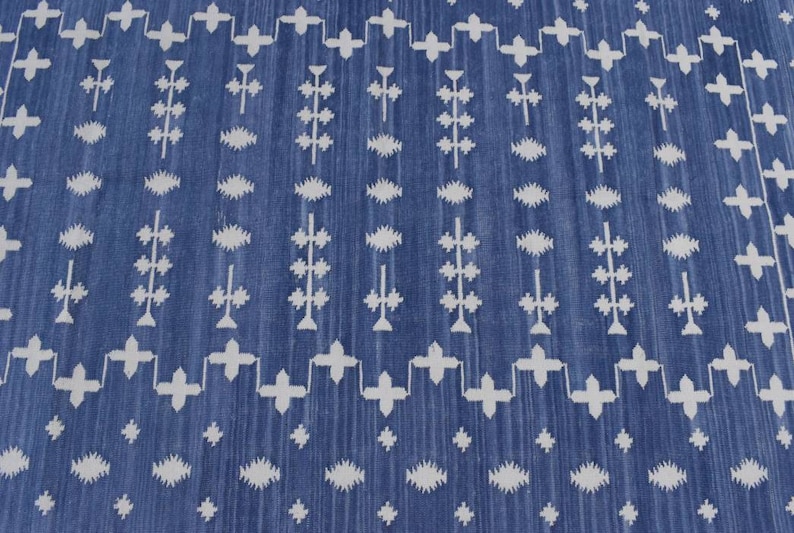 Puede incluir: Una alfombra azul y blanca con un dise&ntilde;o geom&eacute;trico. La alfombra tiene un patr&oacute;n repetitivo de cruces blancas, diamantes y l&iacute;neas verticales sobre un fondo azul.