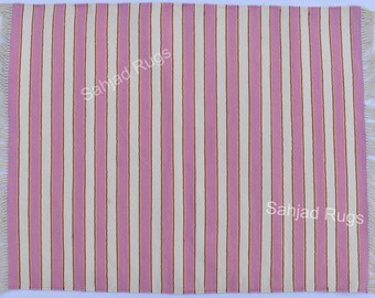 May include: A rectangular rug with vertical stripes in light pink and off-white, accented with thin gold lines. The rug has fringed edges and the text "Sahjad Rugs" is visible. This rug is suitable for home decor.