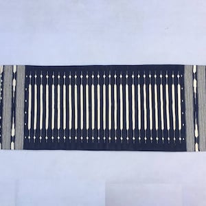 May include: A long, narrow navy blue rug with a white geometric pattern. The rug has a fringe on both ends.
