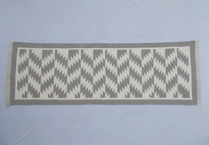 Op de afbeelding: Een grijze en witte geometrisch gepatroneerde loper met franjes.
