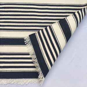 May include: A black and white striped rug with fringe on all sides. The rug is folded in half, showing the underside.