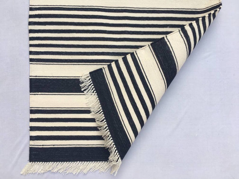 May include: A black and white striped rug with fringe on all sides. The rug is folded in half, showing the underside.