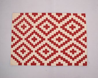 May include: Red and white geometric patterned rug with a diamond pattern.