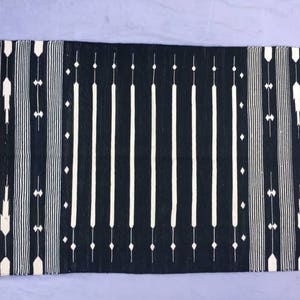 May include: Black and white striped rug with a geometric pattern. The rug has fringe on all four sides.