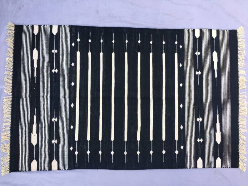 May include: Black and white striped rug with a geometric pattern. The rug has fringe on all four sides.