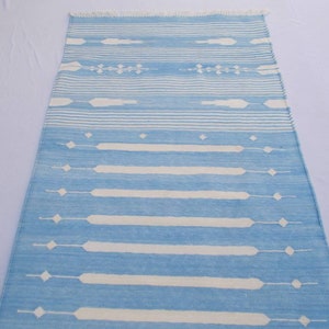 Puede incluir: Una alfombra de rayas azules y blancas con un patr&oacute;n geom&eacute;trico. La alfombra tiene un borde con flecos.