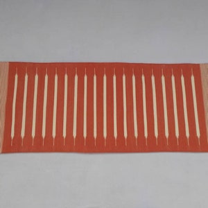 May include: A red and white striped runner rug with a geometric pattern. The rug has a fringe on both ends.