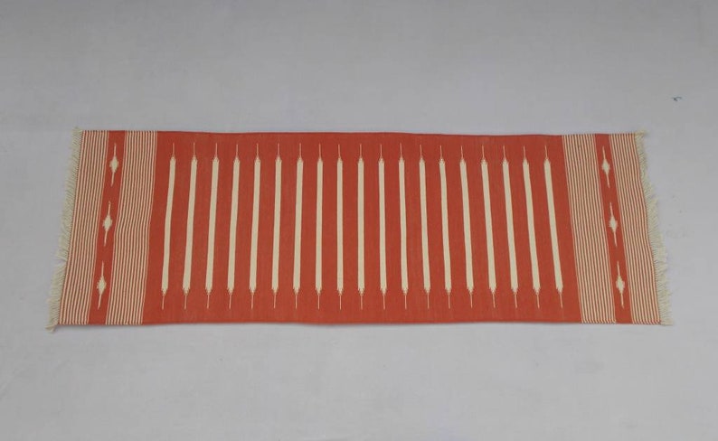 May include: A red and white striped runner rug with a geometric pattern. The rug has a fringe on both ends.