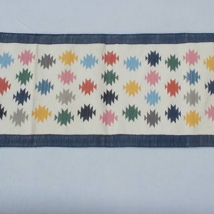 May include: A white runner rug with a blue border and a repeating pattern of colorful geometric shapes.