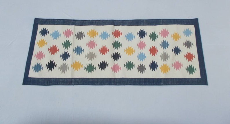 May include: A white runner rug with a blue border and a repeating pattern of colorful geometric shapes.