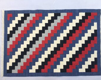 May include: A blue, red, black, white, and gray geometric patterned rug with fringe on all sides.