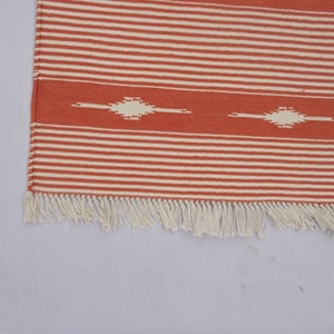 May include: A red and white striped rug with a white fringe. The rug has a geometric pattern in the center.
