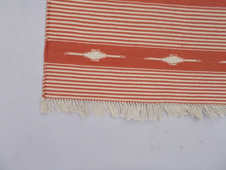 May include: A red and white striped rug with a white fringe. The rug has a geometric pattern in the center.
