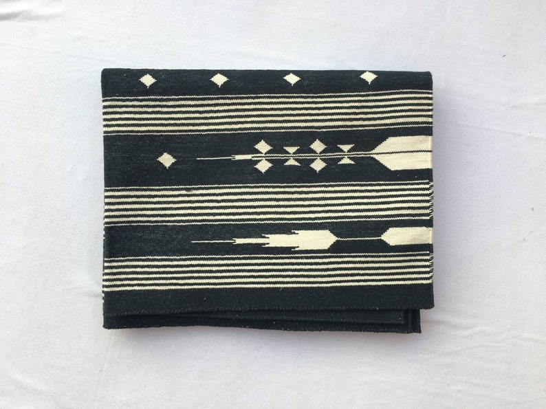 K&ouml;nnte beinhalten: Gefaltetes schwarz-wei&szlig; gewebtes Textil mit geometrischem Muster. Das Design zeigt horizontale Streifen, Rauten und pfeilartige Motive. Das Textil ist gefaltet und zeigt seine Textur und sein Design.
