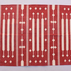 May include: Red and white cotton rug with a geometric pattern. The rug has a fringe border.