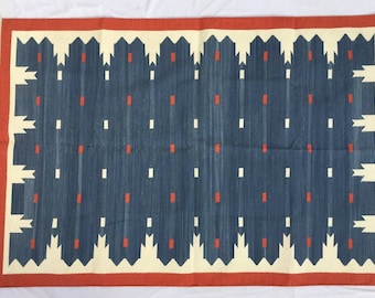 May include: A blue and white woven rug with a red border. The rug has a geometric pattern with white squares and red rectangles.
