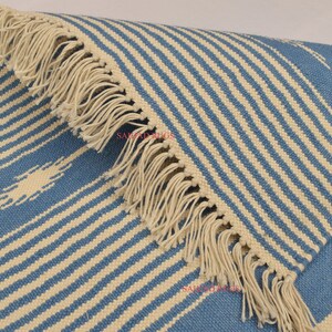 May include: Blue and cream striped rug with fringed edges. The rug features a repeating pattern of diagonal stripes in light blue and cream. The fringed edge adds a decorative element to the rug.