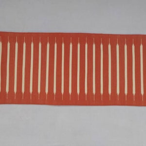May include: A red and white runner rug with a geometric pattern. The rug has a fringe on both ends.
