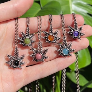 May include: Seven silver necklaces with a leaf-shaped pendant featuring a different coloured gemstone in the centre. The gemstones are green, orange, purple, blue, pink, black, and light blue.