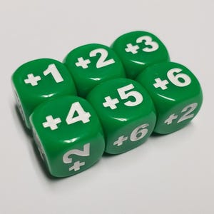 May include: Six green dice with white numbers and plus signs. The dice are arranged in a group, with numbers ranging from +1 to +6. The dice are likely used for board games or role-playing games.