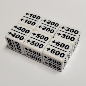 以下が含まれることがあります： 黒い文字が書かれた白いサイコロ7個セット。各サイコロには、+100、+200、+300、+400、+500、+600などの異なる数字が記載されています。サイコロは白い表面に配置されています。