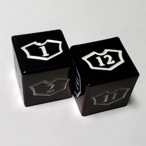 May include: Two black dice with white numbers. The dice are shaped like a shield with rounded edges. The numbers on the dice are 1, 2, 11, and 12.