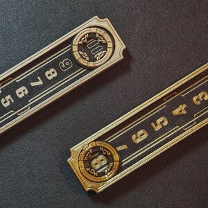 Puede incluir: Dos placas de direcci&oacute;n rectangulares doradas con fondos negros. Cada placa presenta n&uacute;meros dorados y un dise&ntilde;o circular con un n&uacute;mero. Las placas son probablemente para n&uacute;meros de casa o direcciones comerciales.