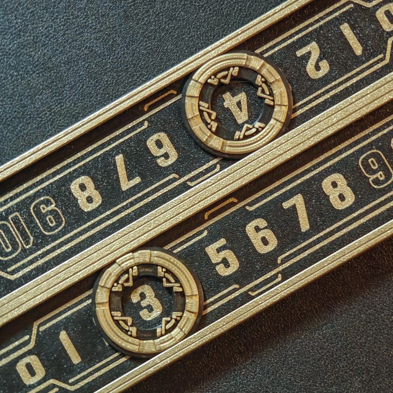 Puede incluir: Primer plano de dos diales num&eacute;ricos negros y dorados con los n&uacute;meros 3 y 4 visibles. Los diales est&aacute;n colocados sobre una superficie negra con n&uacute;meros y l&iacute;neas doradas. El dise&ntilde;o tiene una est&eacute;tica futurista e industrial.