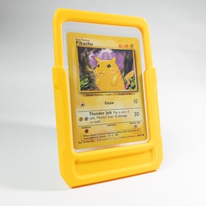 May include: A yellow Pikachu Pokémon card in a yellow protective case. The card features a yellow Pikachu character with the text "Pikachu" and "40 HP". The card is in a clear plastic sleeve.