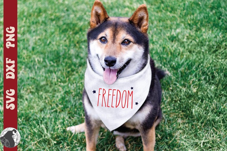 May include: A Shiba Inu dog wearing a white bandana with the word "FREEDOM" in red script and black star accents. The dog has black, brown, and tan fur and is sitting on green grass.