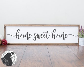 May include: A white wooden sign with a brown frame, featuring the text "home sweet home" in black cursive script.