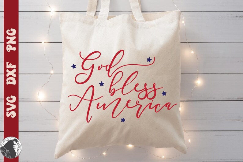May include: A cream-colored tote bag with the words "God bless America" in red script and blue star accents. The bag is made of a sturdy fabric and has two handles.