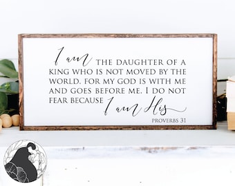 May include: A framed sign with a white background and black text. The text reads: "I am the daughter of a king who is not moved by the world. For my God is with me and goes before me. I do not fear because I am His." The bottom of the sign reads "Proverbs 31".