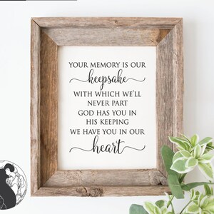 May include: A framed print with a rustic wooden frame. The print features elegant black script that reads "Your memory is our keepsake... We have you in our heart." Decorative greenery is visible in the lower right corner.