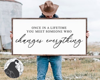 May include: A wooden sign with the text "Once in a lifetime you meet someone who changes everything" in black script font.