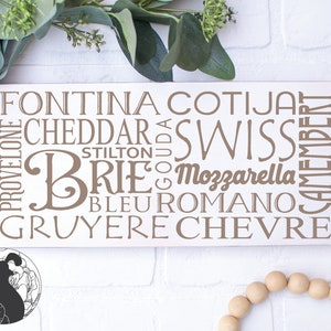 Puede incluir: Un letrero de madera blanco con las palabras "Fontina, Cotija, Cheddar, Swiss, Brie, Mozzarella, Bleu Romano, Gruyere, Chevre, Provolone, Stilton, Gouda, Camembert" escritas en texto marr&oacute;n.