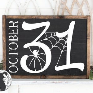 May include: A rectangular wooden sign with a black background and white lettering. The sign reads "OCTOBER" vertically on the left side and "31" with a spider web and spider design. The frame is a dark brown color.