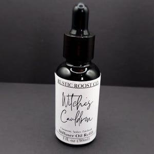 May include: A black glass bottle with a dropper top, labeled "Witches Cauldron" from Rustic Roost Co. The label lists cinnamon, amber, and patchouli as ingredients. The bottle contains 1 fl. oz. (30ml) of diffuser oil refill.