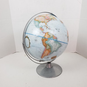 May include: A vintage globe with a light blue ocean and colorful continents. The globe is mounted on a silver metal stand and held by a silver metal meridian. The globe is a classic educational tool.