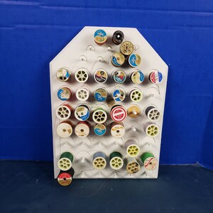 May include: White plastic thread rack with multiple spools of thread in various colors, including red, green, blue, yellow, and white.