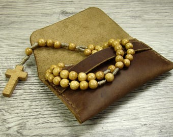 May include: A brown leather pouch with a wooden rosary inside. The rosary has a wooden cross at the end.
