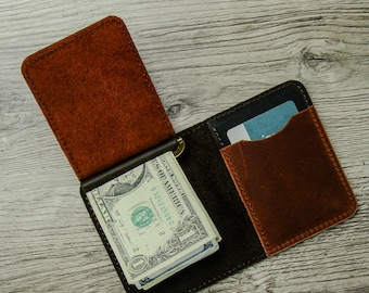 May include: Open leather wallet with a money clip holding several one-dollar bills. The wallet is brown and black with a card slot and a separate brown leather pocket. The wallet is open, displaying the contents.