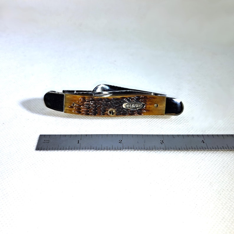 May include: A closed pocket knife with a brown handle and a silver blade. The knife has a Case logo and is next to a ruler. The handle appears to be made of a textured material.