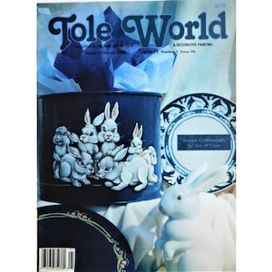 May include: The cover of "Tole World" magazine features a dark blue container with a painted scene of white rabbits. A white ceramic rabbit figurine is in the foreground. The magazine's title is in large, stylized letters.