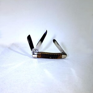 May include: A pocket knife with three open blades. The knife has a brown handle with a textured pattern and silver-colored metal accents. The blades are shiny and reflect the light. The knife is set against a white background.