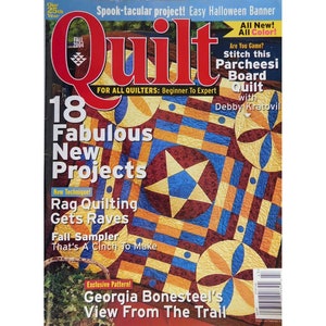 May include: The cover of a quilting magazine, featuring a colorful quilt design with geometric patterns in shades of blue, gold, and burgundy. Text includes "Quilt" and "18 Fabulous New Projects."
